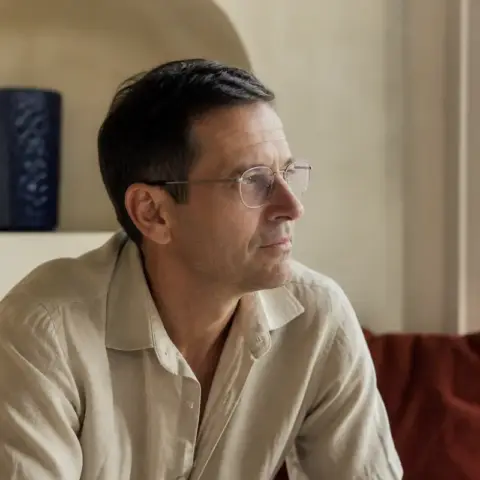 Retrato de Gonzalo Echegaray, pelo negro corto con algunas canas y gafas de montura fina, camisa de lino color arena