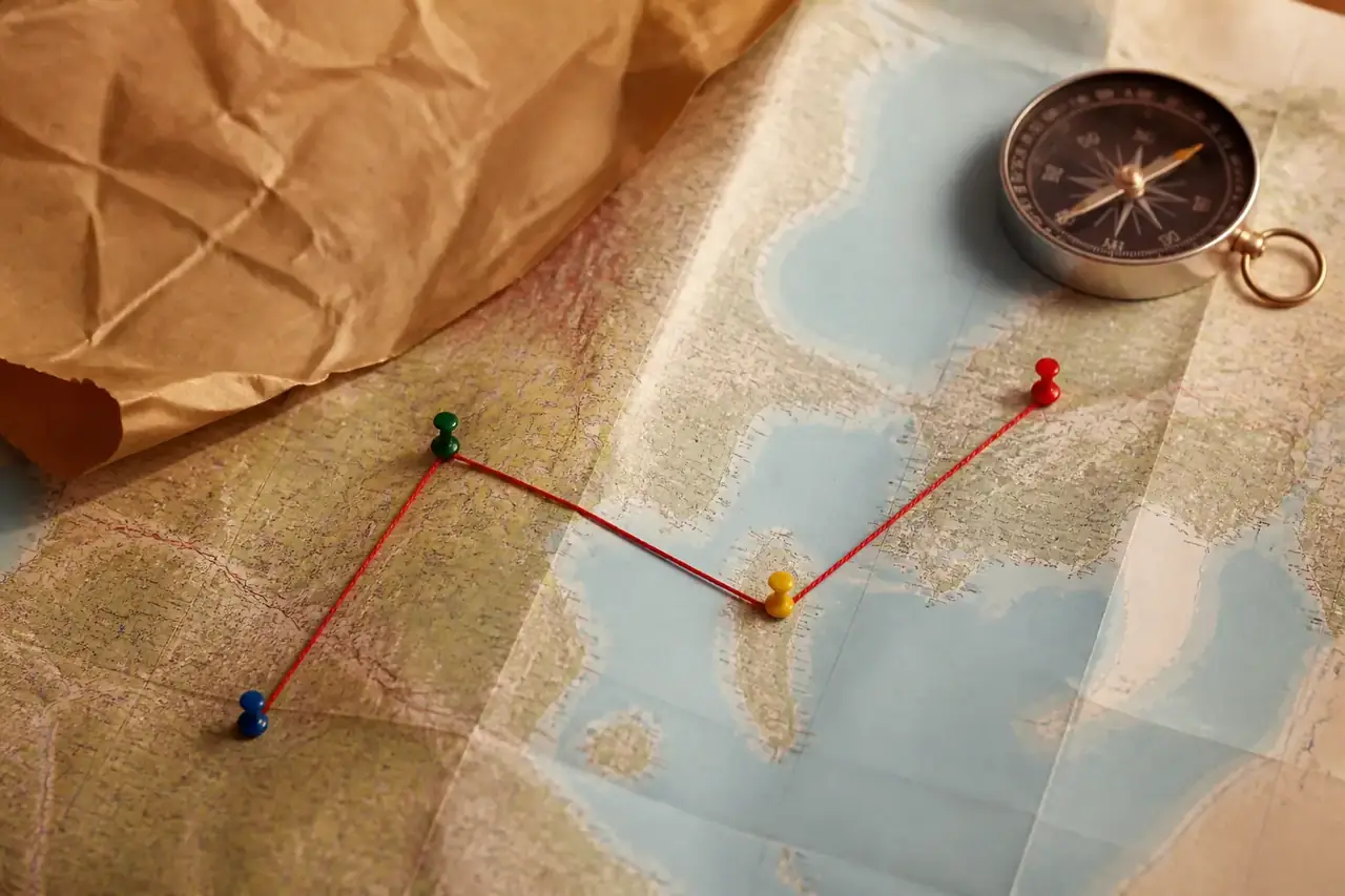 Papel kraft con una brújula, chinchetas de colores y un hilo rojo trazando una ruta sobre un mapa